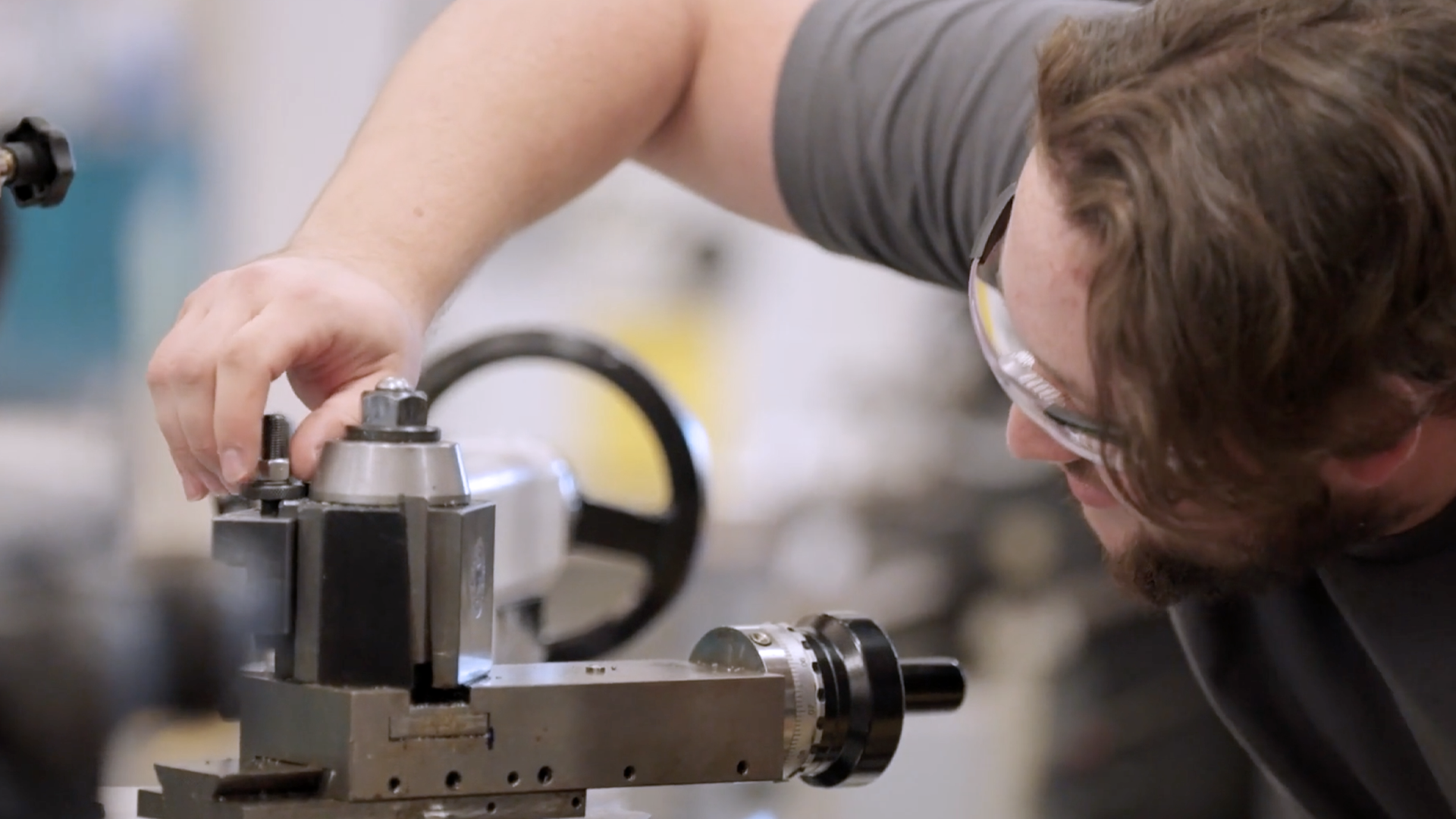 Student adjusting a metal lathe machine while wearing safety glasses in a workshop.
