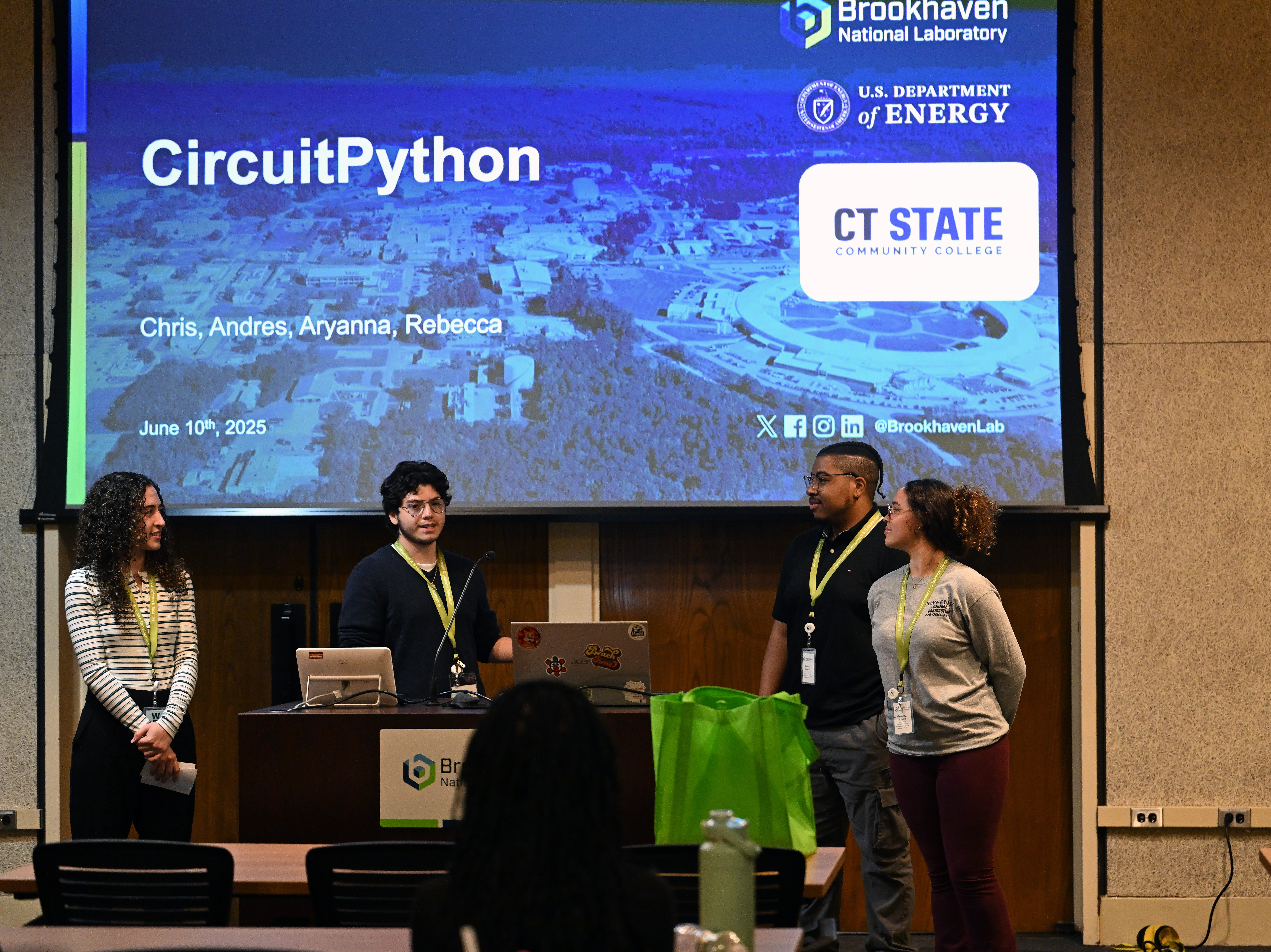 Four students stand in front of a large projection screen.