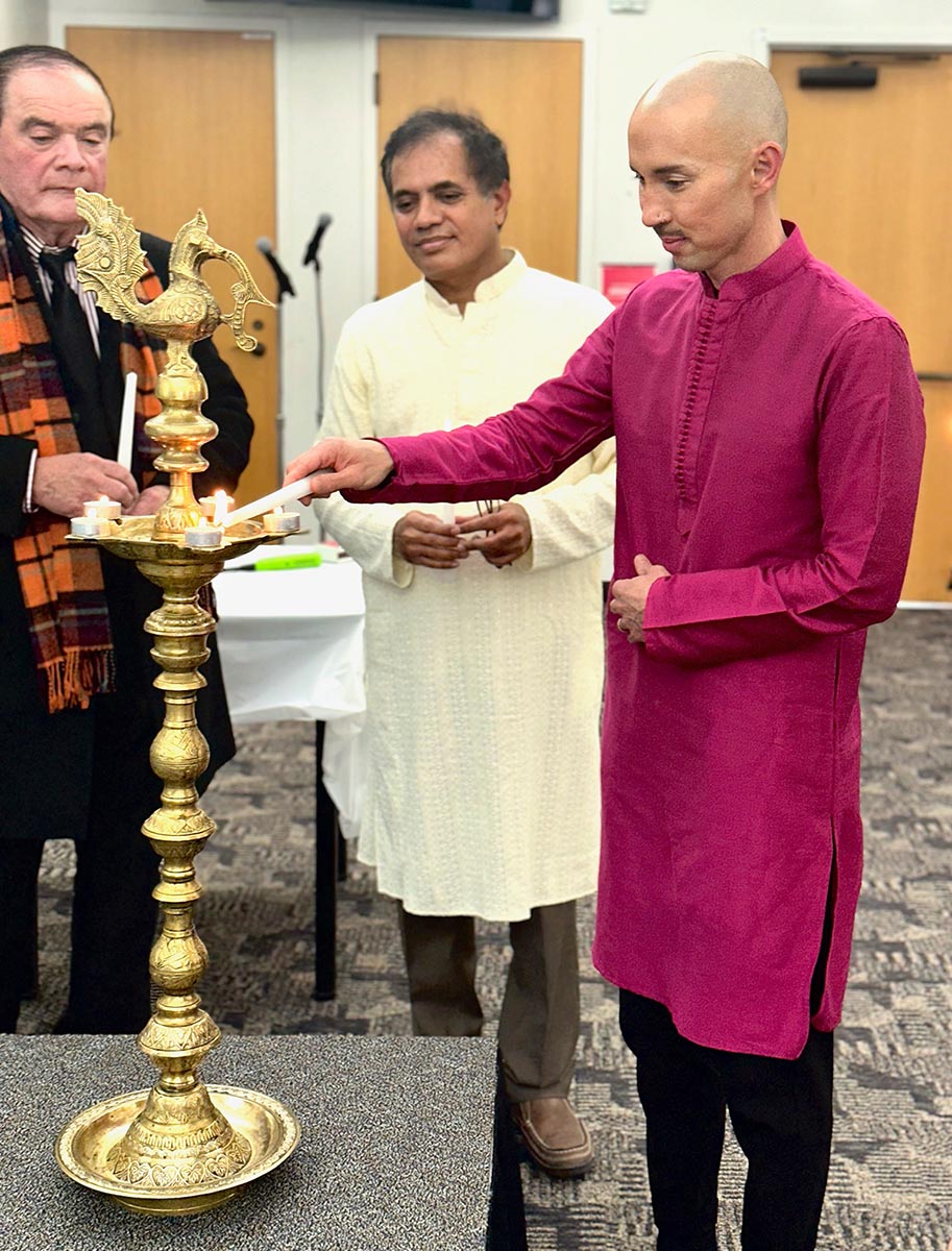 Person in magenta kurta lighting a traditional brass oil lamp at a celebration event