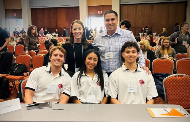 4 students sit at a table with a male professor