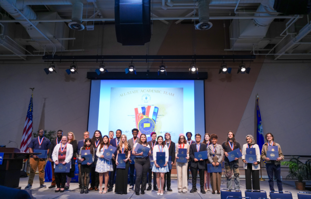 A group of students stand on a stage smiling and holding certificates.