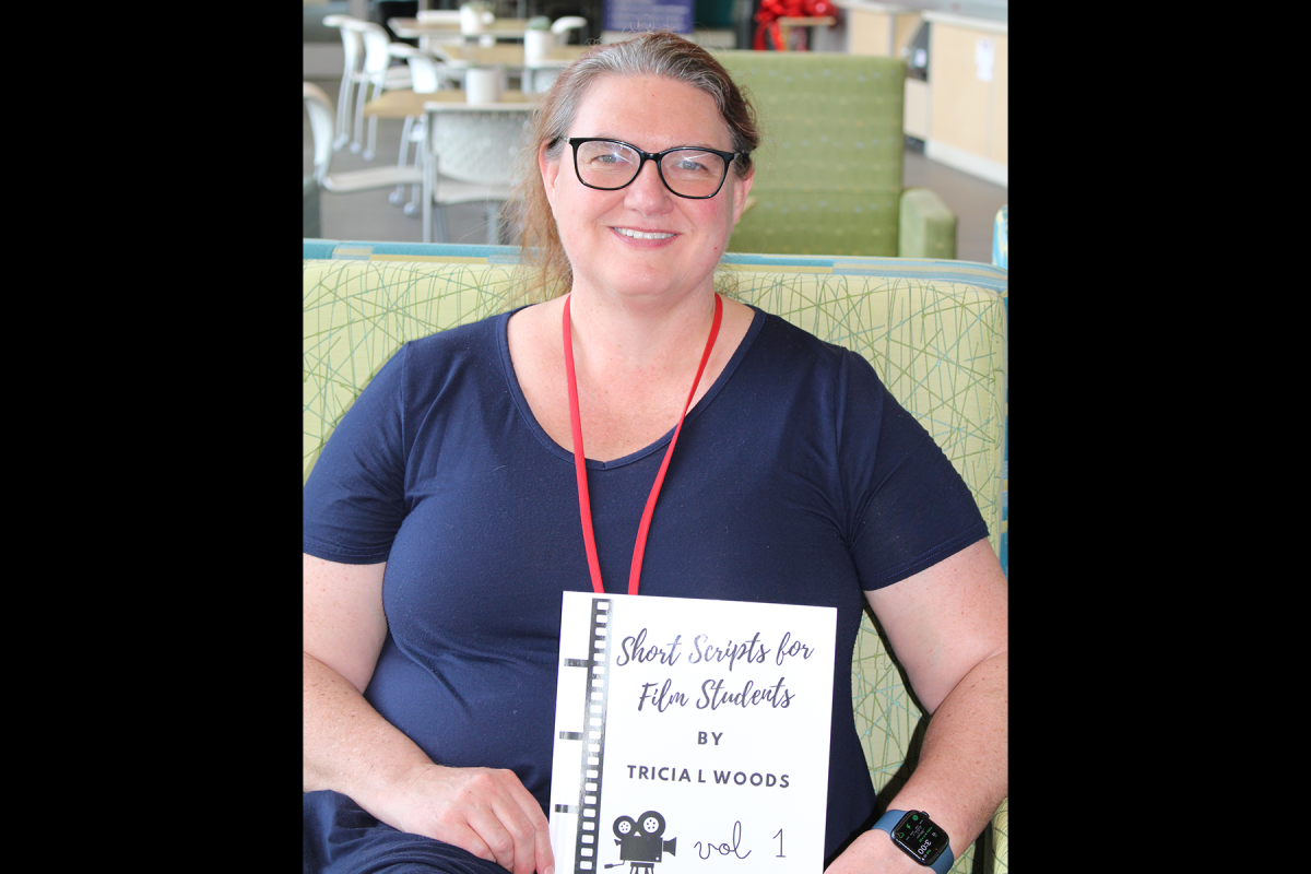 Intructor holds book while seated and smiling.
