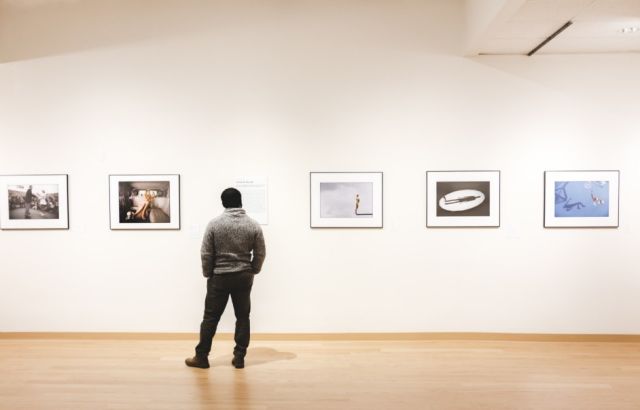 Man stands in front of a line of photographs lining the wall
