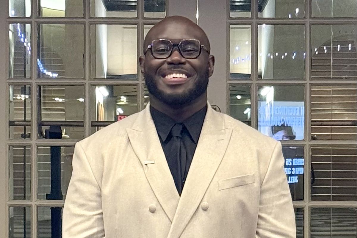 Jordan Long smiles into the camera in a white suit jacket.