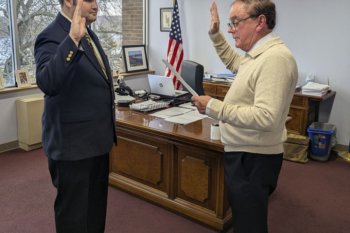 Man holds up hand to be sworn in as he faces another man.
