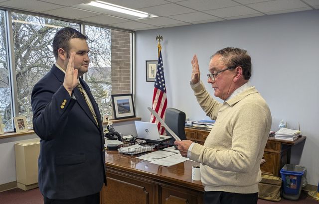 Man holds up hand to be sworn in as he faces another man.