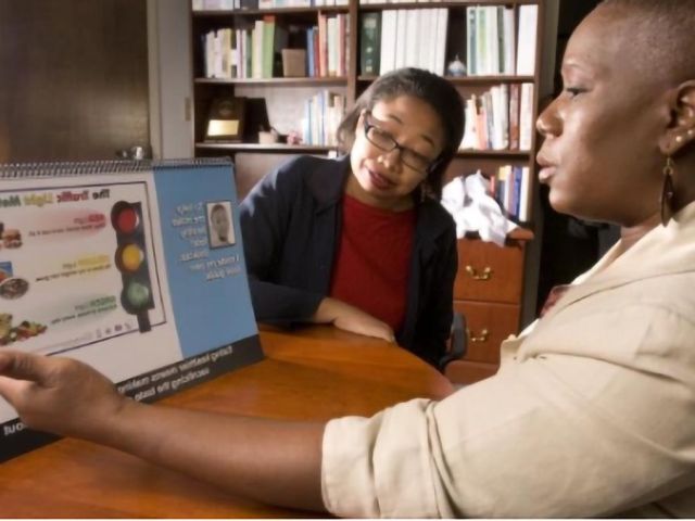 Community public health educator uses a nutrition education display to teach a participant about healthy food choices.