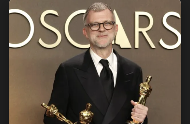A man stands in front of a background depicting the word Oscars